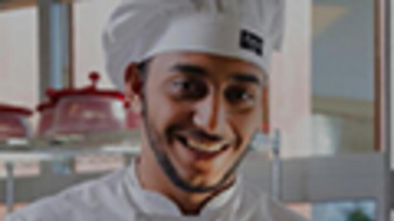 Een student kok staat vrolijk in de keuken