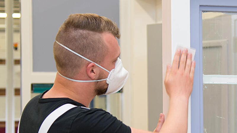 Een schilder schuurt een kozijn in de praktijkruimte