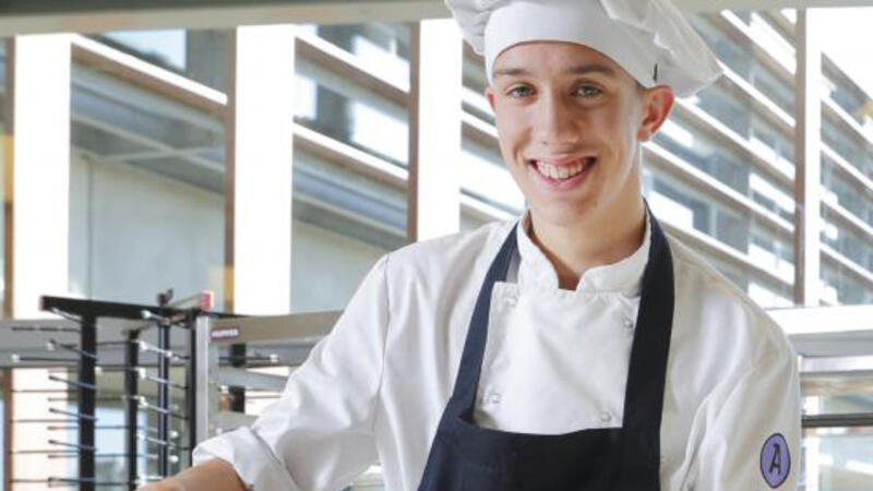 Een student kok staat vrolijk in de keuken