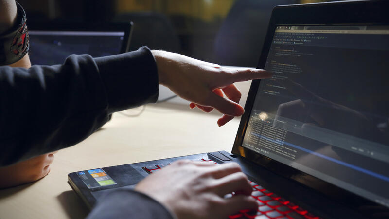 Iemand zit achter een laptop en wijst naar het beeldscherm