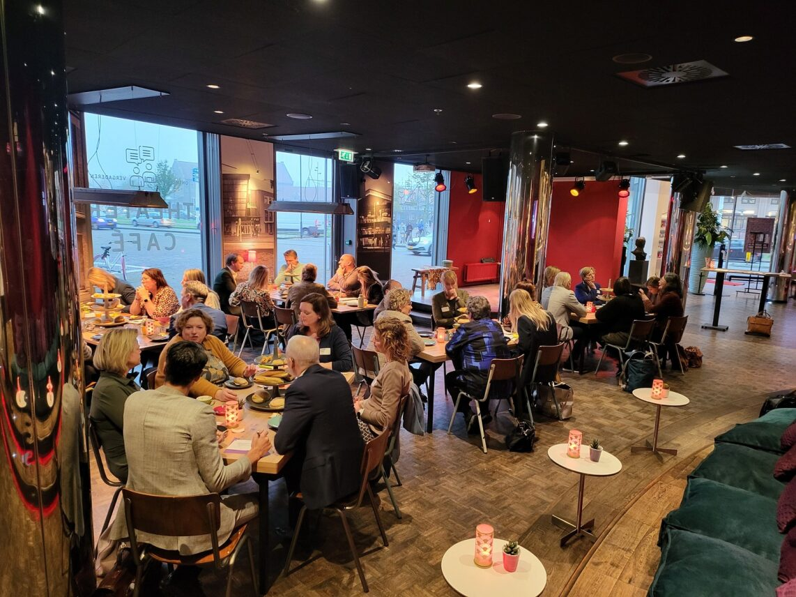 Aanwezigen zitten gezellig aan tafeltjes in het theater café in de Deventer Schouwburg