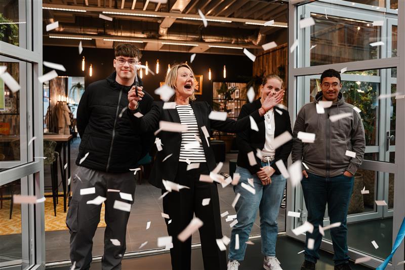 Ellen Marks staat met drie studenten bij de ingang van Spees in Apeldoorn en knip een lintje door terwijl de confetti in de lucht vliegt
