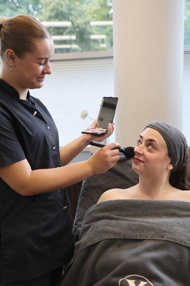 Een jongedame geeft een gezichtsbehandeling aan een klant in een schoonheidssalon