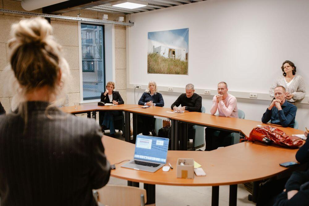 Een dame geeft een presentatie in een ruimte met mensen zittend aan een tafel
