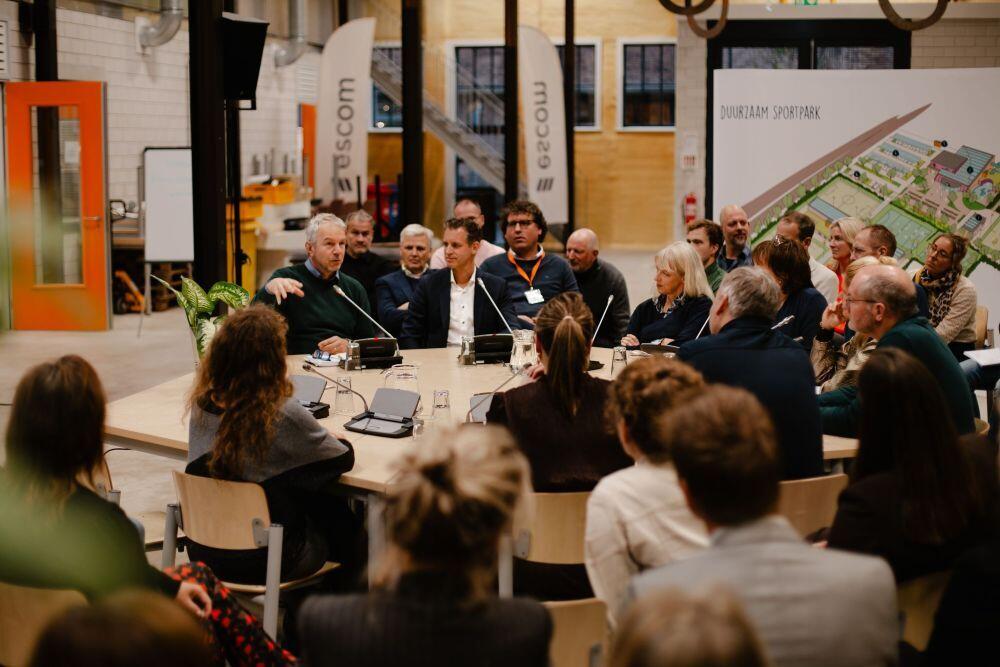 Aan een ronde tafel zitten mensen die met elkaar praten