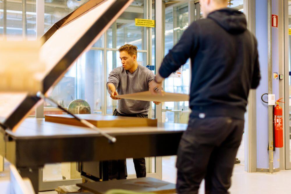 Twee studente Hout & Meubel leggen een houten plaat op een zaagtafel