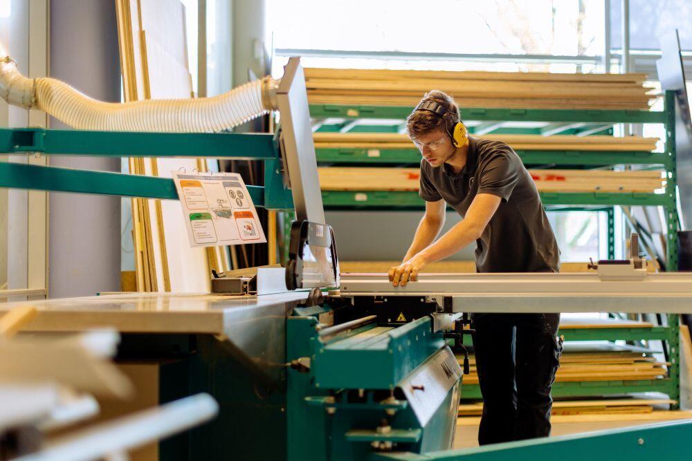 Een student Hout & Meubel is zaagt hout op een zaagtafel 