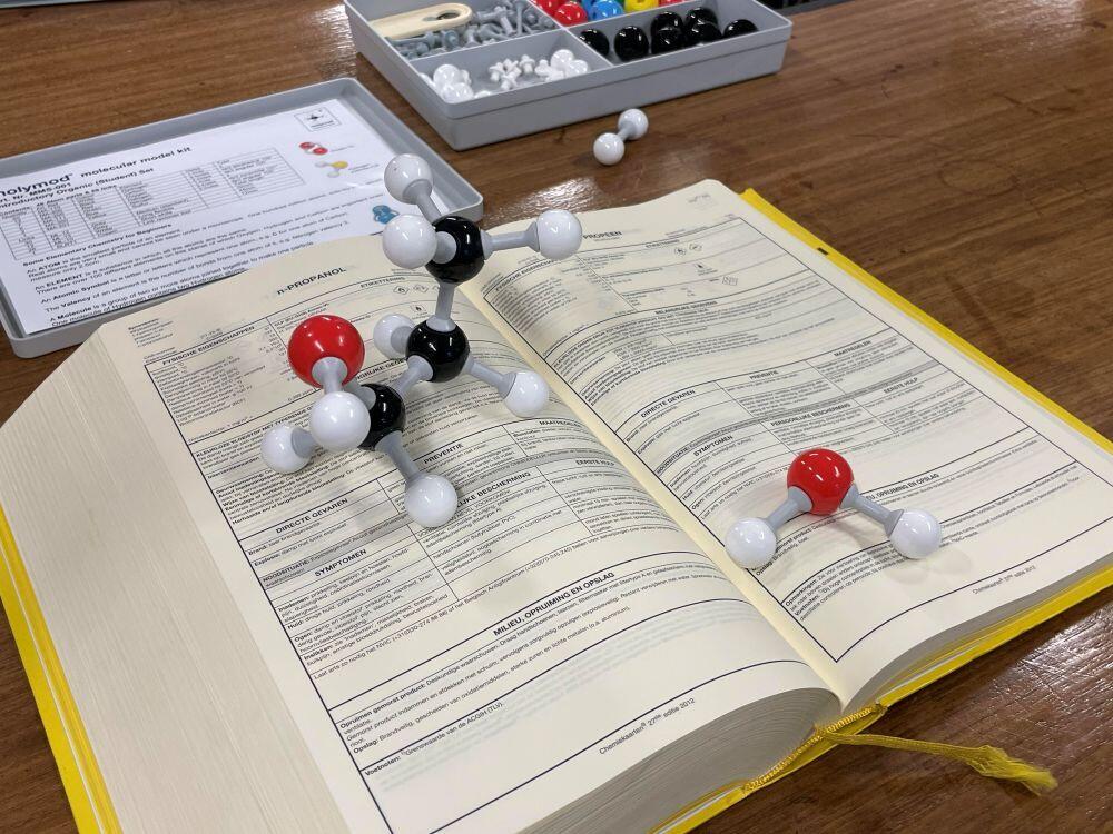 Een dik boek met beschrivingen van chemische verbindingen ligt opengeslagen op een tafel, een model van propanol ligt op de bladzijde van propanol
