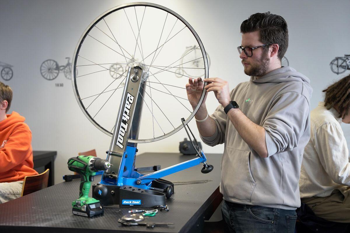 Een jongeman voert werkzaamheden uit aan de spaken van een fietswiel