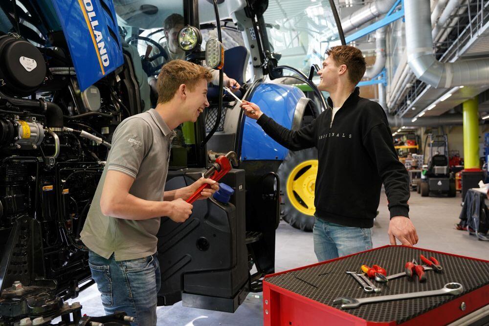 Drie Landbouwtechniek-studenten zijn bezig met gereedschappen bij een trekker
