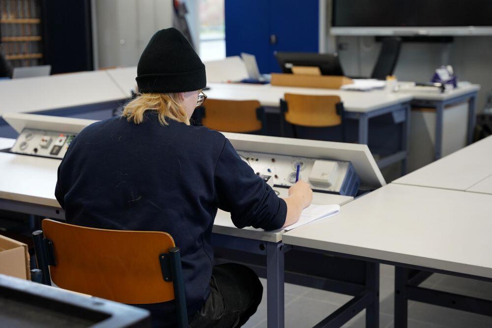 Een student Autotechniek zit in een praktijkruimte en maakt aantekeningen