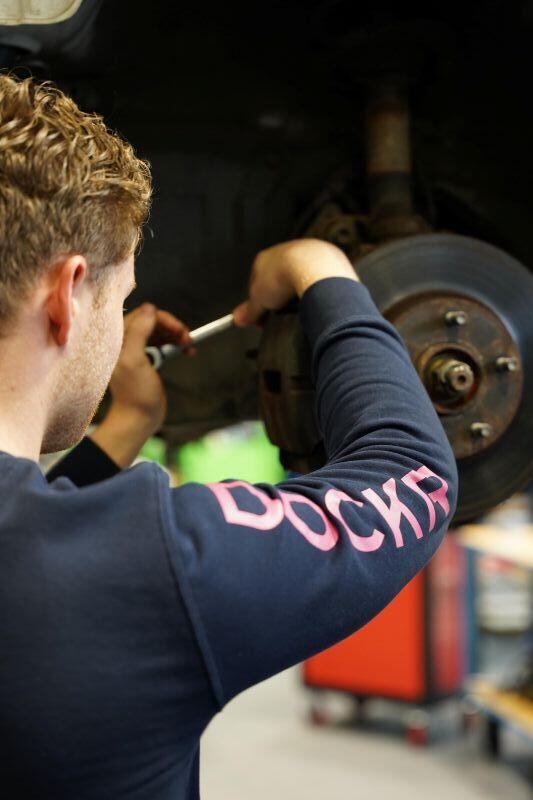 Een student Autotechniek sleutelt aan een wiel van een auto op een brug