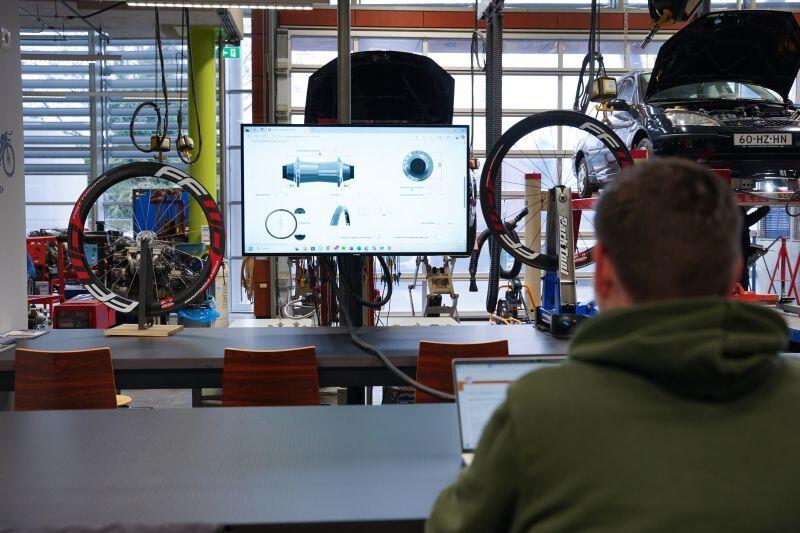 Een student fietstechniek zit in het praktijklokaal en kijkt naar een presentatie op een groot beeldscherm