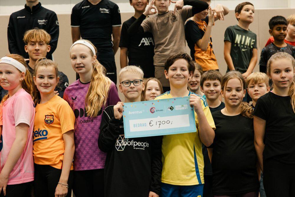 Een groep kinderen in een gymzaal laat een cheque zien ter waarde van € 1.700