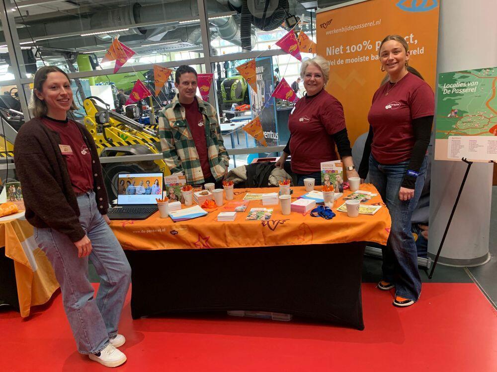 Vier medewerkers van een zorg- & welzijn-instelling staan bij hun stand in de Hi-Street in de locatie Laan van de Mensenrechten in Apeldoorn