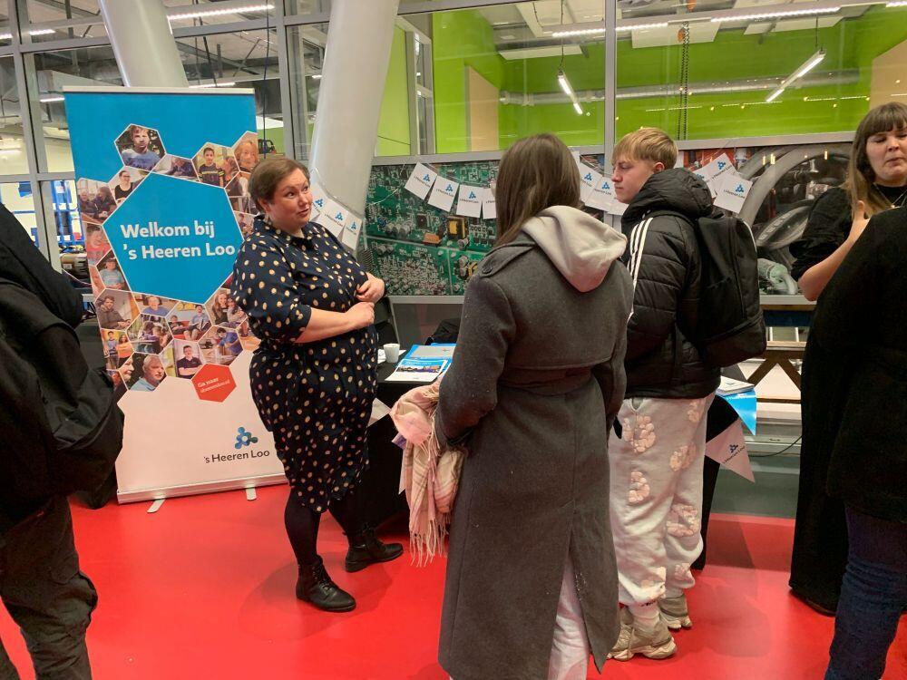 Een dame van een zorg- & welzijn-instelling geeft toelichting aan twee studenten