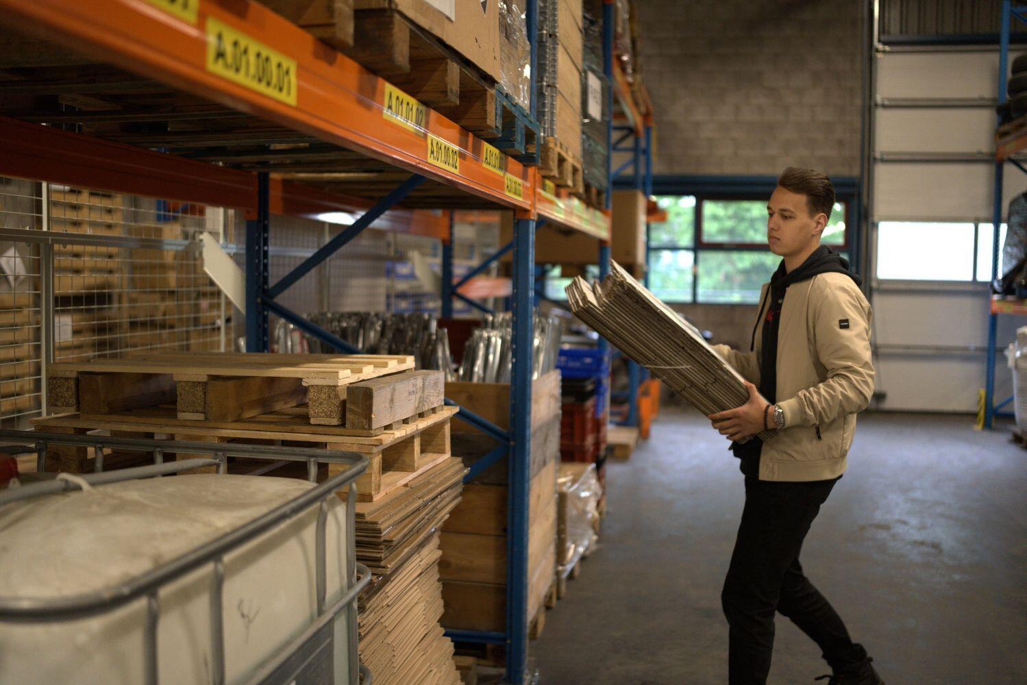 Een magazijnmedewerker loopt in een magazijn met een stapel dozen