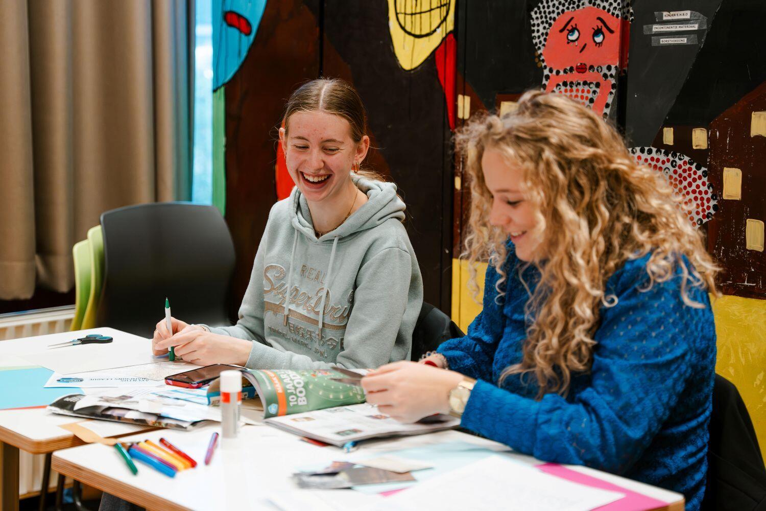 Twee studentes zitten lachend te knutselen aan een tafel