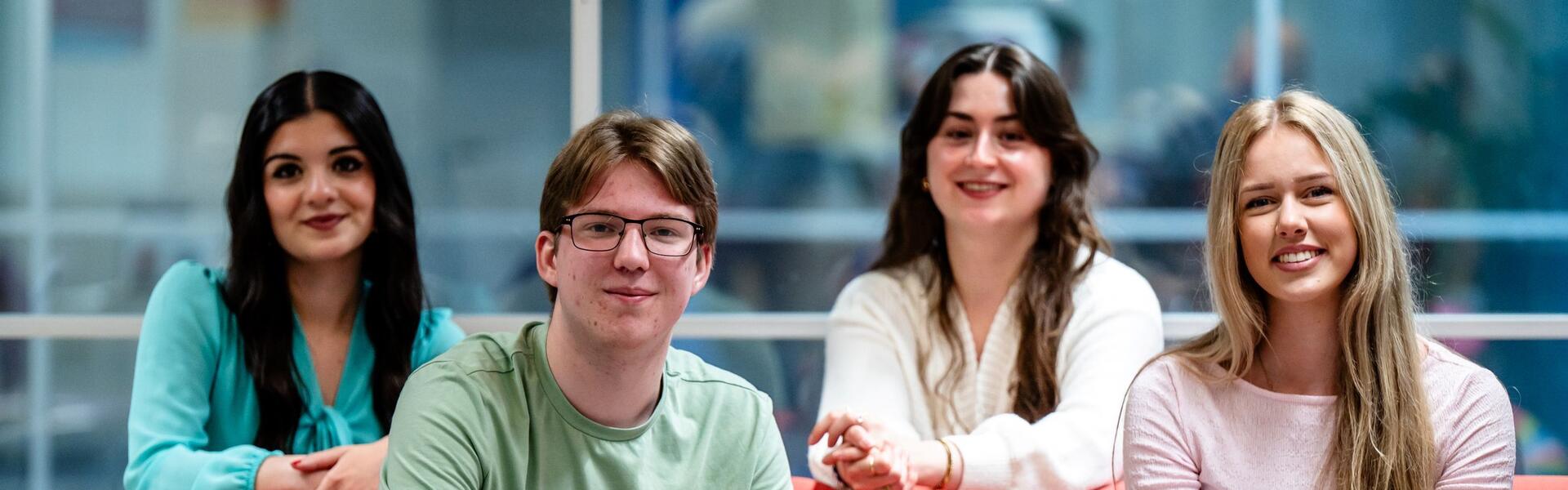 Vier studenten poseren op een rode bank