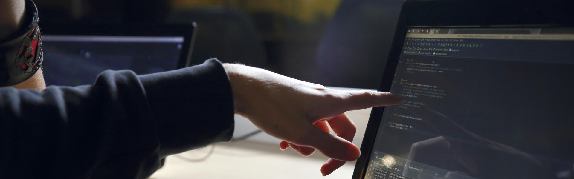 Iemand zit achter een laptop en wijst naar het beeldscherm