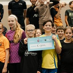 Een groep kinderen in een gymzaal laat een cheque zien ter waarde van € 1.700