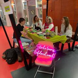 Vier personen zitten gezellig aan een tafel met allerlei promotiemateriaal