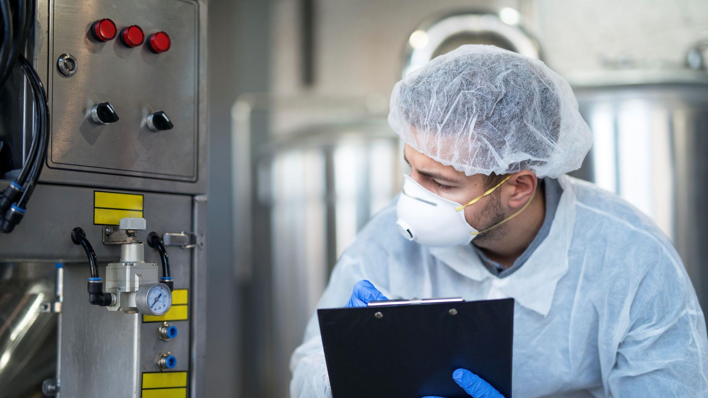 Man met beschermende kleding controleert een machine in een fabriek